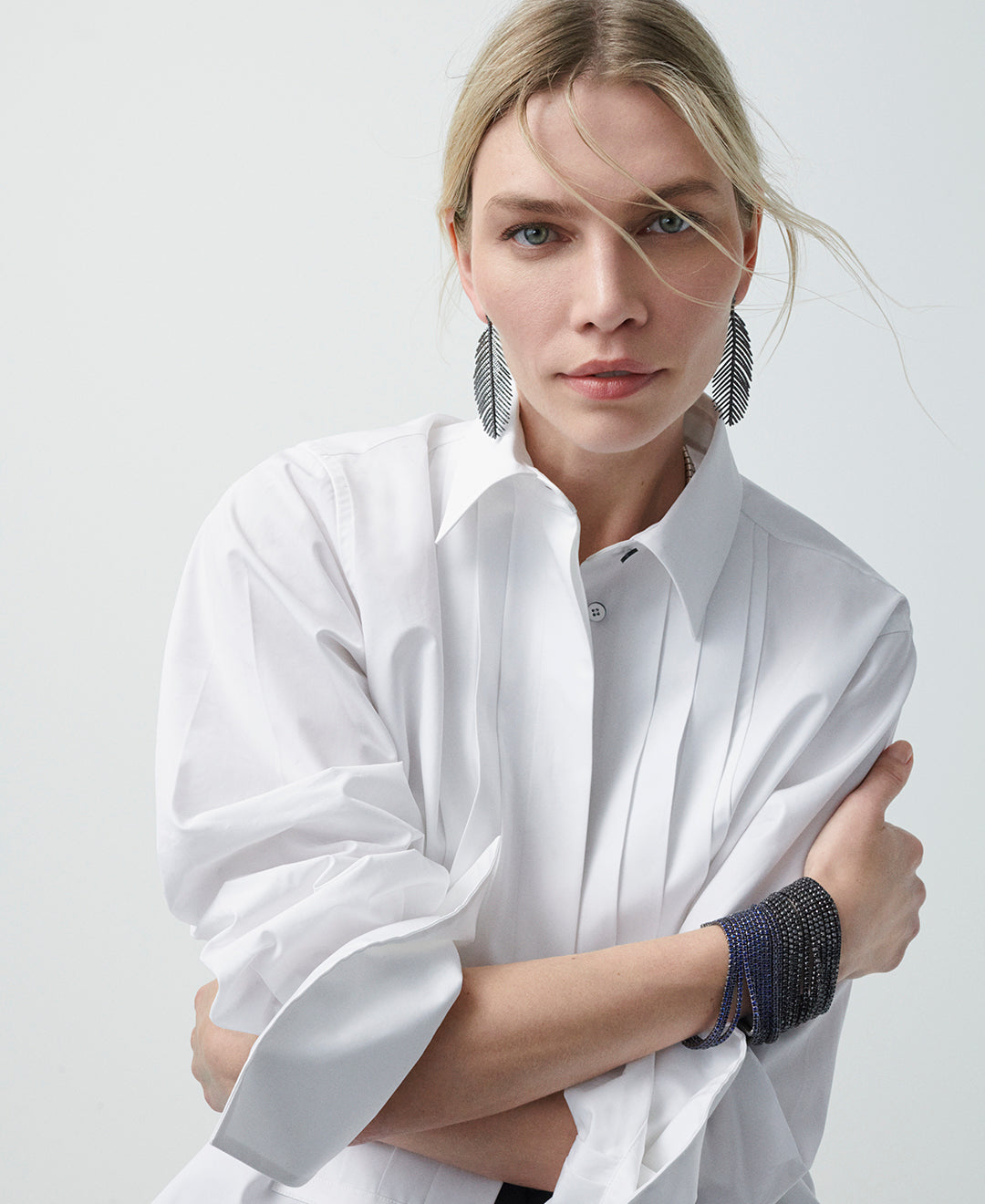 A model wearing a white button down shirt with black diamond Feathers that Move Earrings and a stack of two 11 Row Bracelets with.