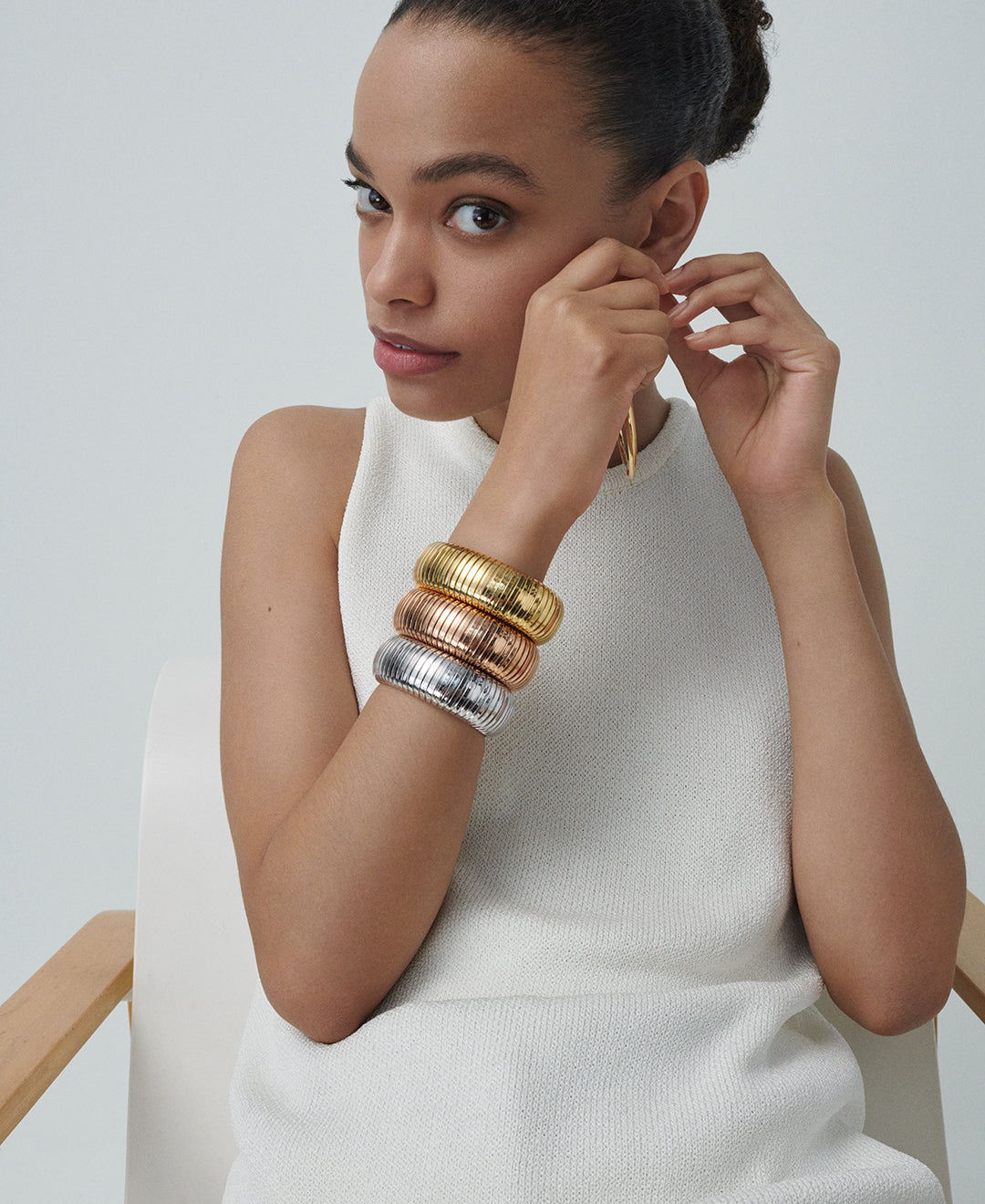 A model is wearing three domed cuffs, one in yellow gold, one in rose gold and one in white gold on her right arm. She is also fastening a Carine Hoop in her left ear.