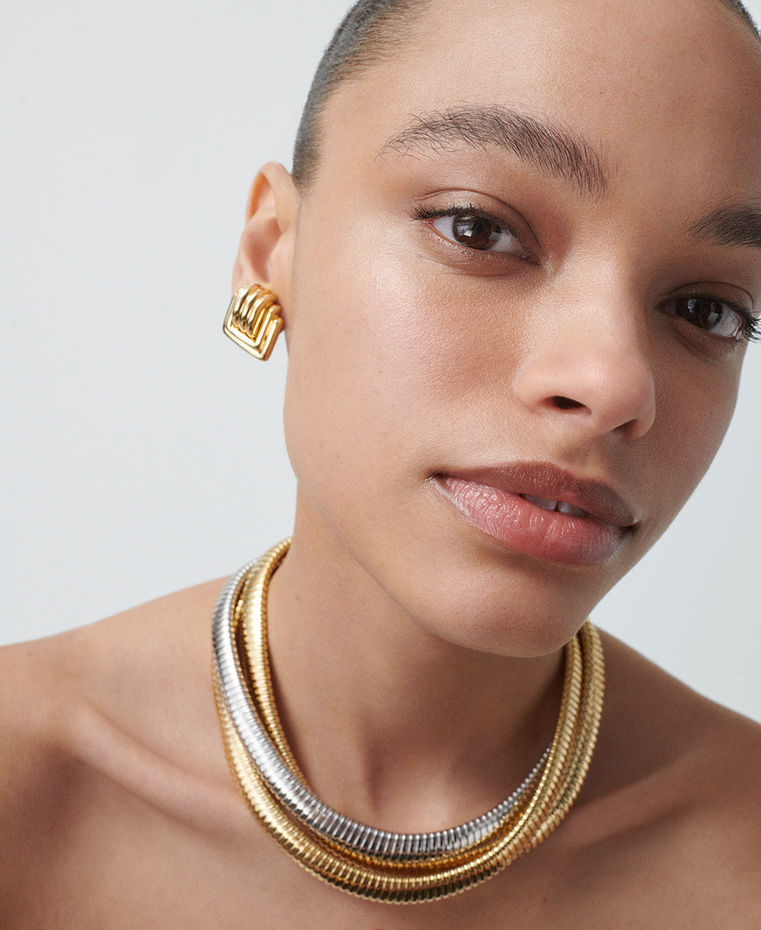 A model wearing yellow gold Square Earrings and a Tre Collana D'Oro Necklace in yellow gold, white gold and rose gold.