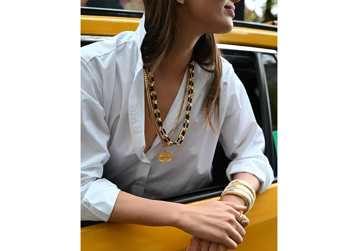 A model is wearing an ebony and gold link necklace, three domed cuffs, a serpentine ring, a tab chain necklace and a zodiac pendant - all in 18k yellow gold.