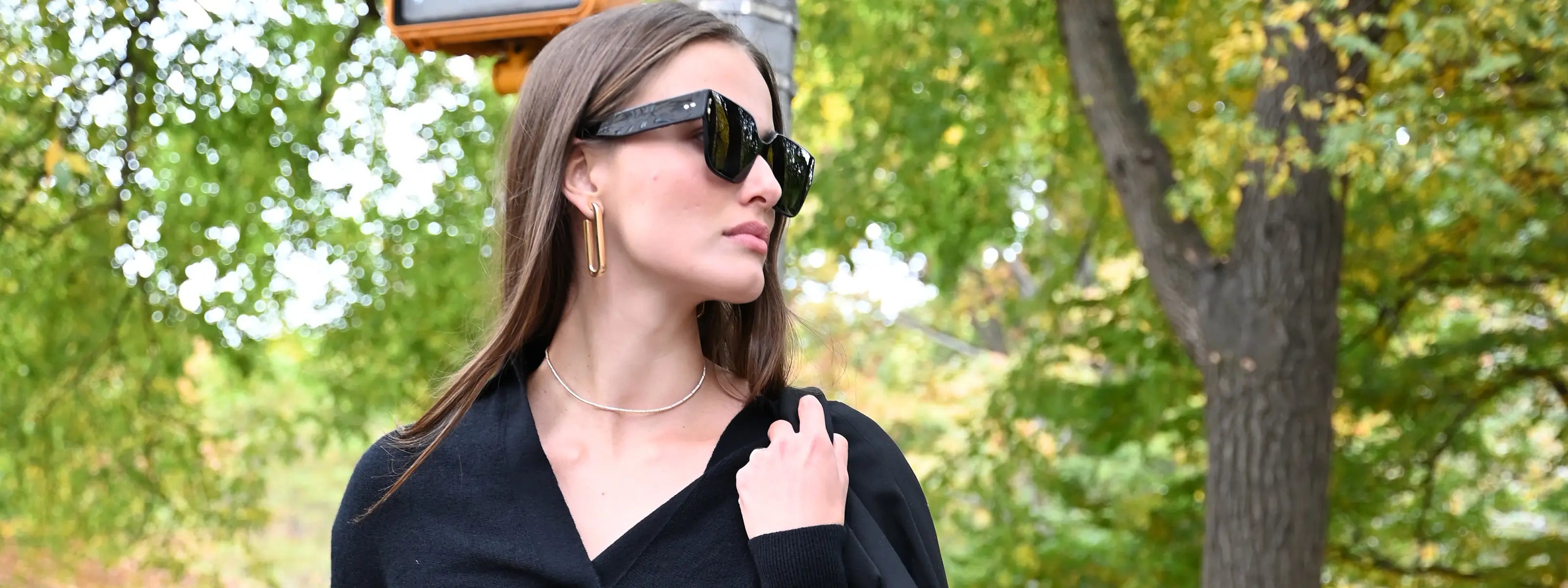 A model is wearing sunglasses and paper clip hoop earrings in yellow gold.