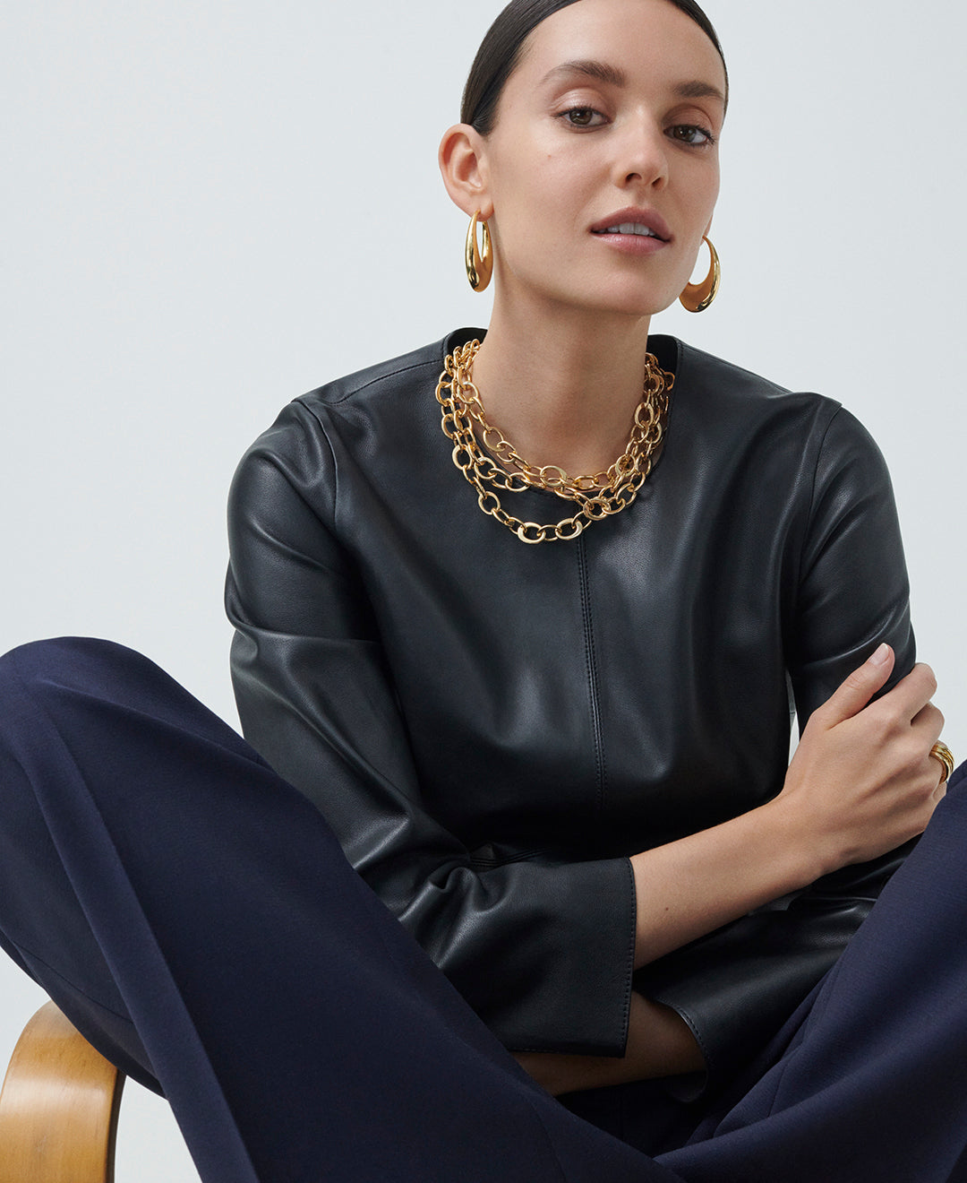 A model is wearing a yellow gold crescent necklace and two gold carine hoop earrings. 