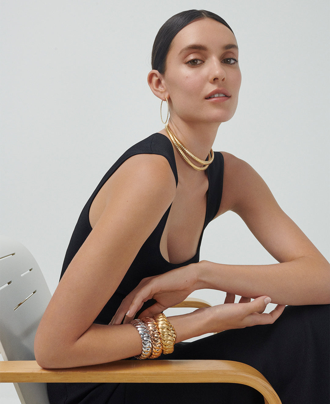 A model is wearing a yellow gold  Collana D'Oro Necklace, three wave link bracelets - in rose, yellow and white gold - and a pair of perfect hoops with diamonds in yellow gold. 