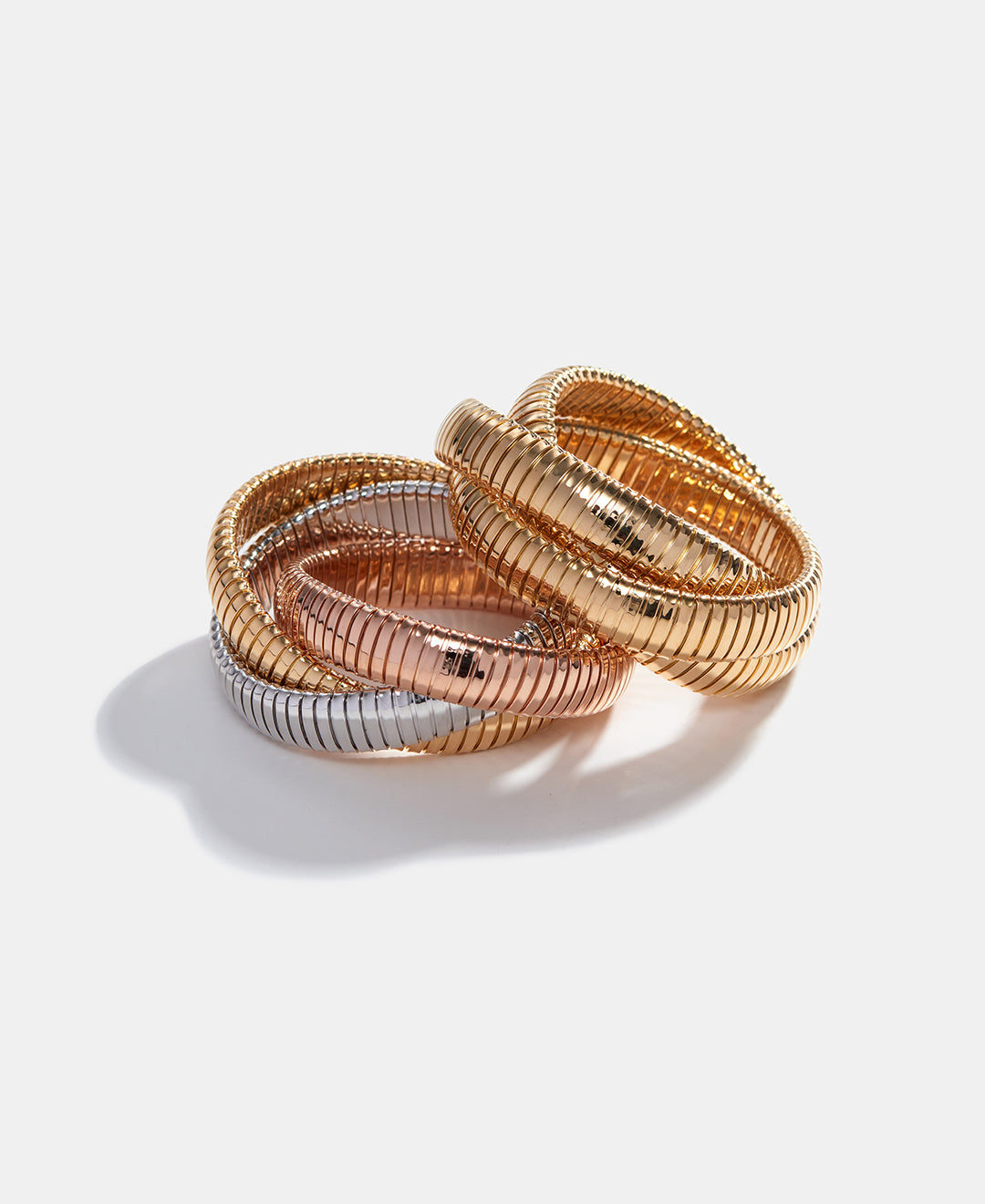Rolling bracelets in yellow gold and a mix of yellow, white and rose gold are stacked askew on a white background.