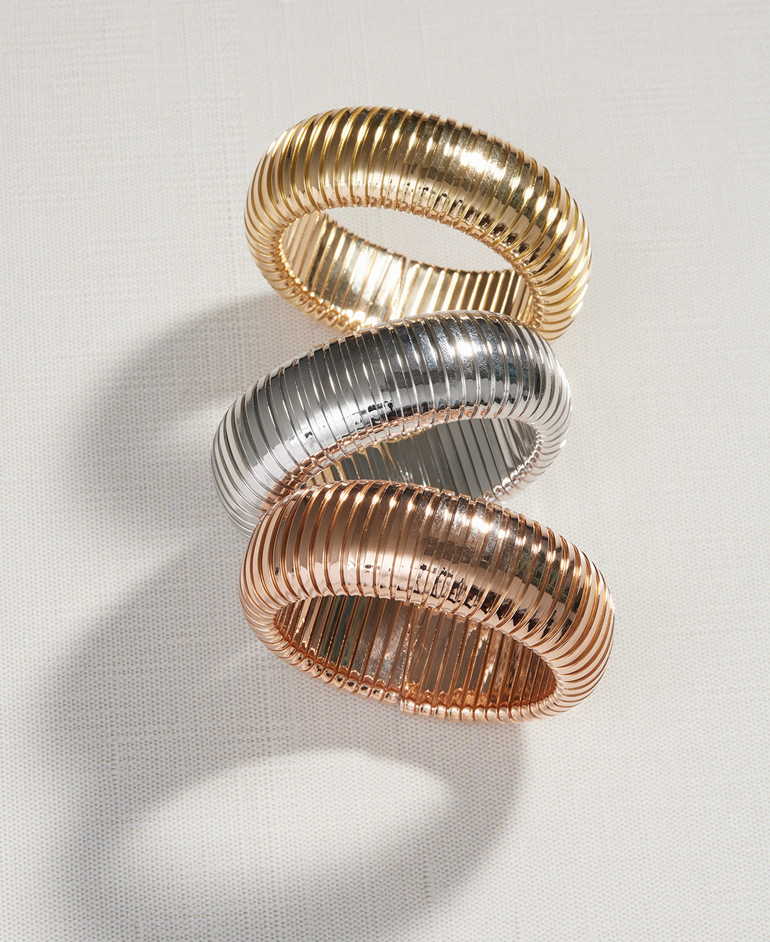 Three domed cuffs, one in yellow gold, one in white gold and one in rose gold are displayed on a white background.