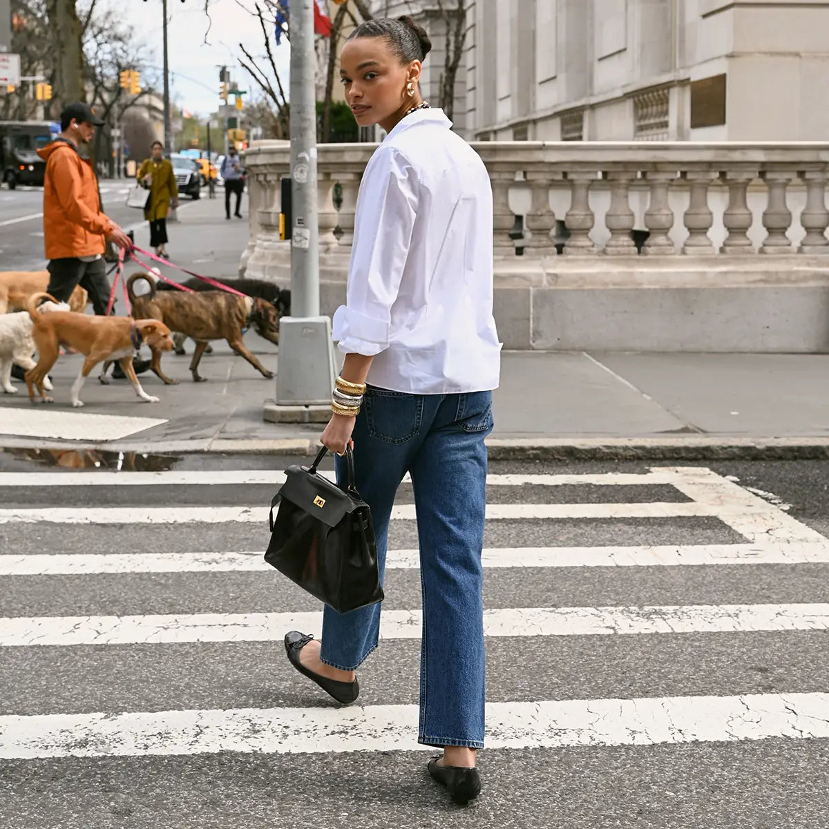 A model is wearing a white shirt, jeans, yellow gold grooved anjou earrings, and domed cuffs in yellow, white and rose gold. 