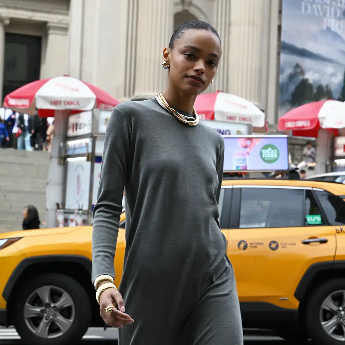 A model is wearing a long knit dress and crossing the street. She is also wearing yellow and white gold swirl earrings, ophelia necklaces in white yellow and rose gold, a stretch line bracelet in yellow gold, a domed cuff in yellow gold, and a passionate panther ring in yellow gold with diamonds.