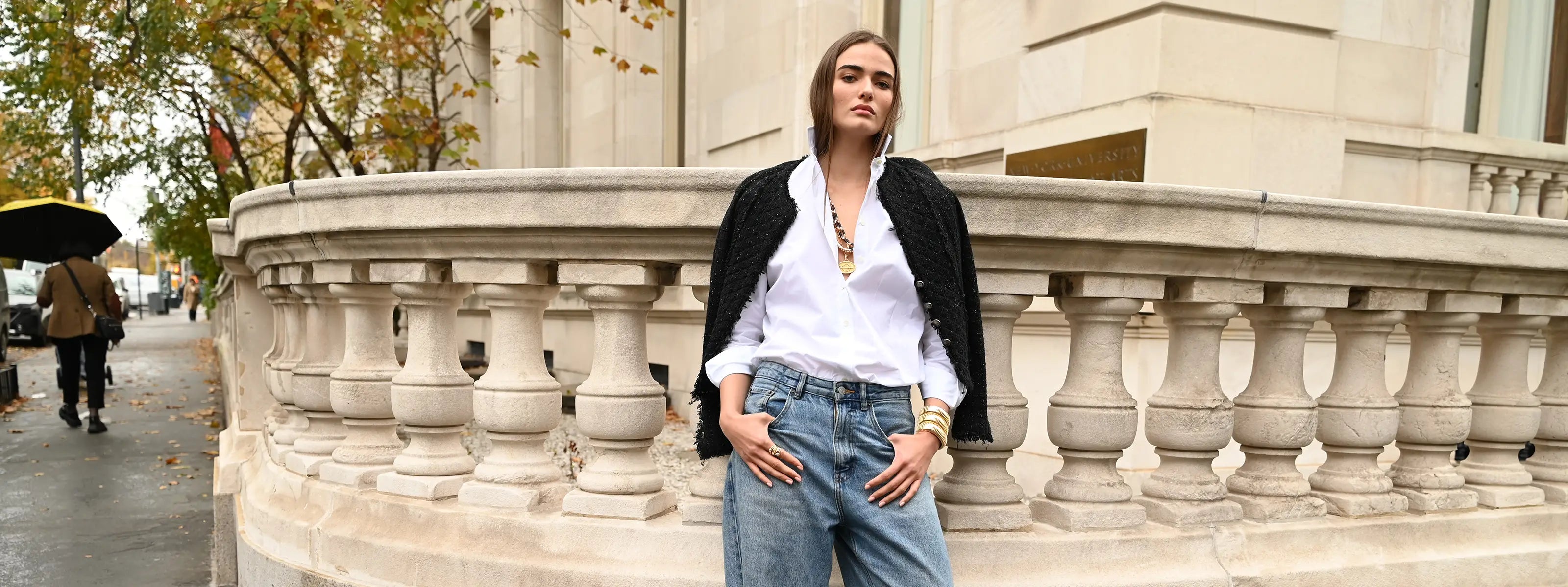 A model is wearing a black jacket, white button down and blue jeans and has on a black and gold links necklace, ophelia necklace, large zodiac pendant, domed cuffs and il serpente rings