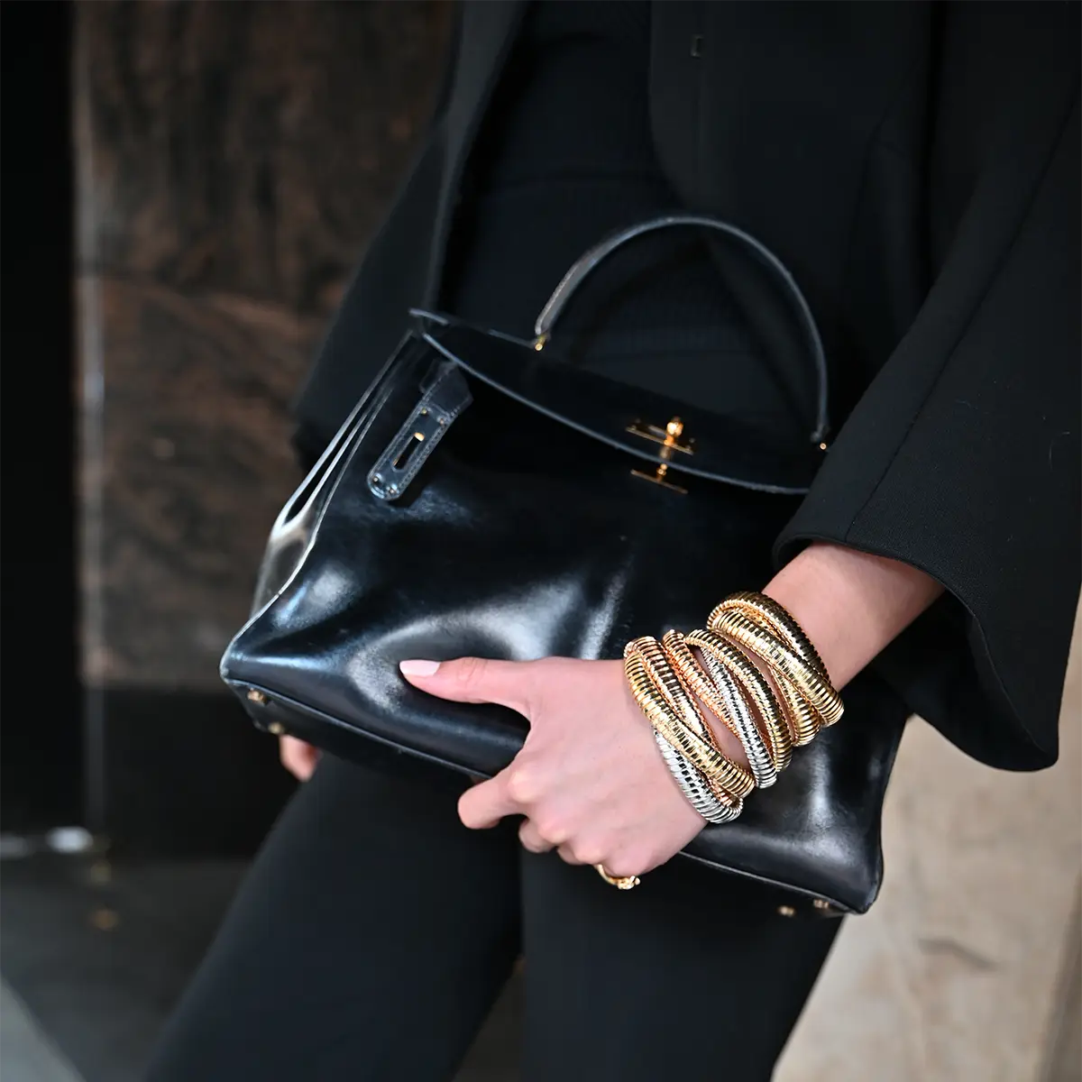 A Closeup of a woman's arm holding a purse. She is wearing three scribble bracelets in yellow, white and rose gold.