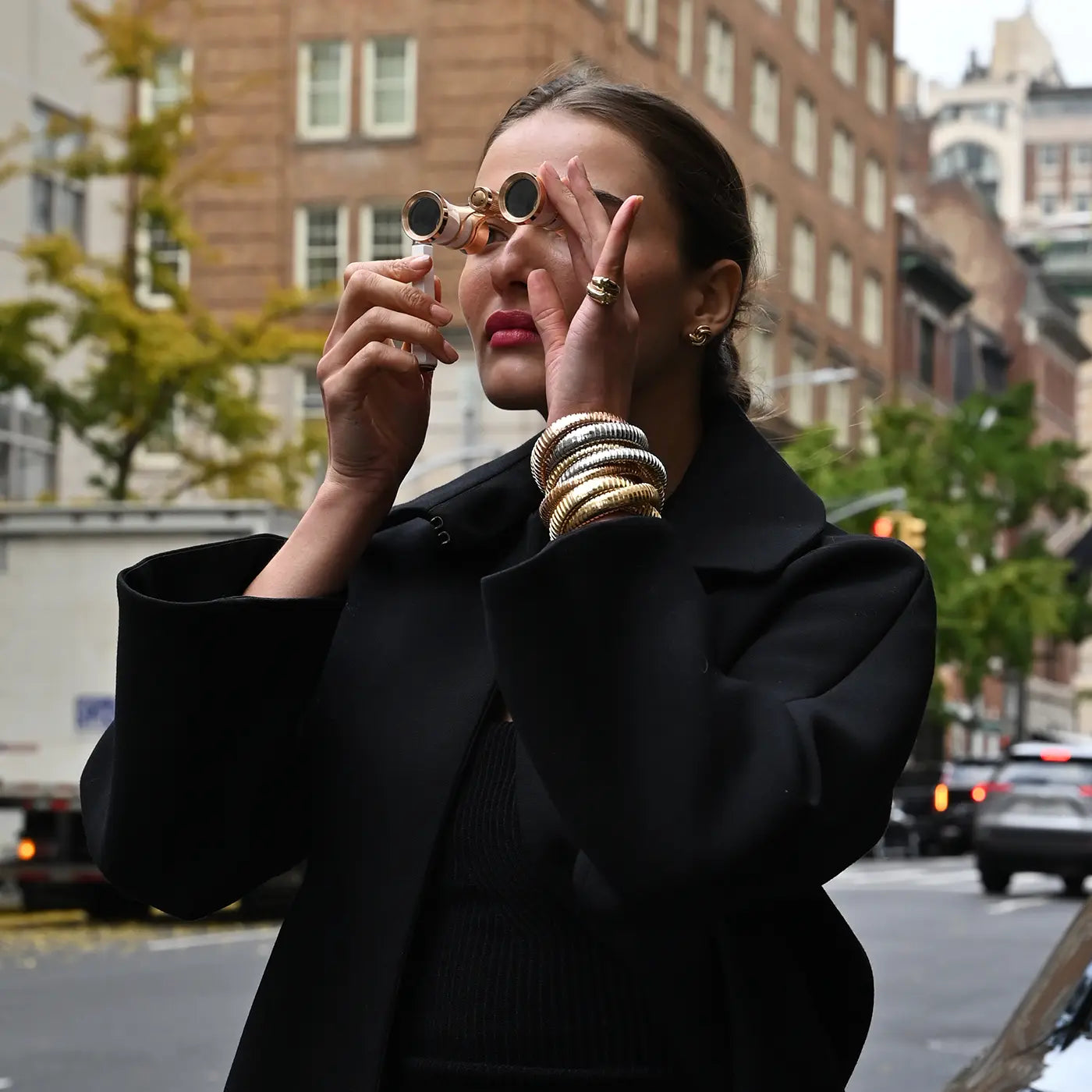 A model looks through opera glasses while wearing a yellow gold passionate panther ring, swirl earrings and rolling bracelets.