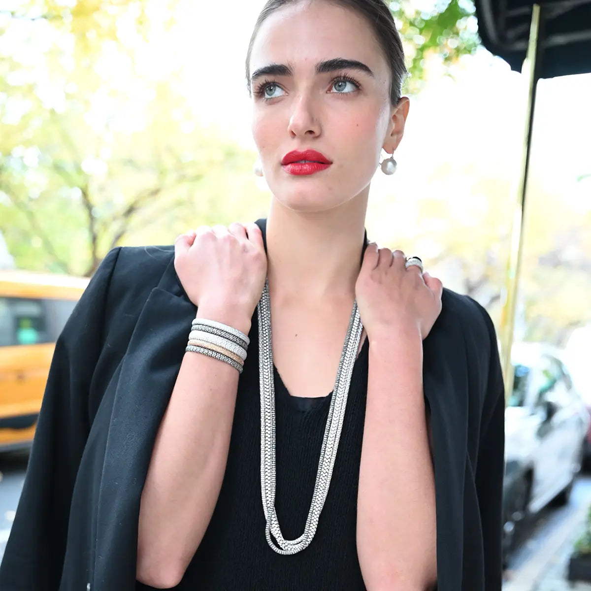 A model is wearing pearl on the hook earrings, a stack of pave stretch bracelets with diamonds, and a group of rope and lunetta necklaces with dieamonds.