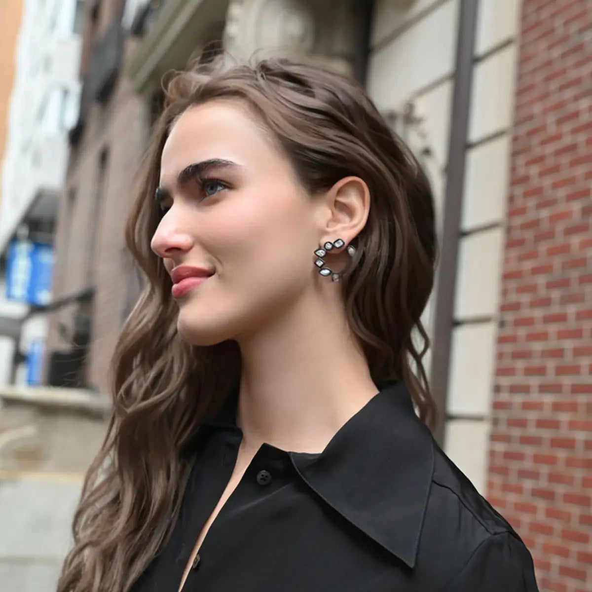 A model is smiling and wearing a black shirt and enamel diamond multi shape earrings.